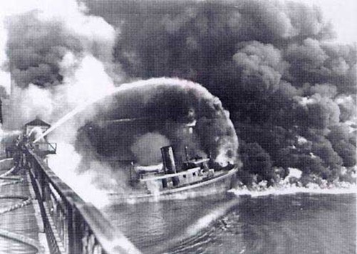 Firemen stand on a bridge over the Cuyahoga River in November 1952 to spray water on the tug Arizona