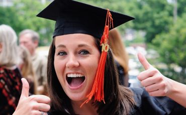 A new graduate indicates success with two thumbs up